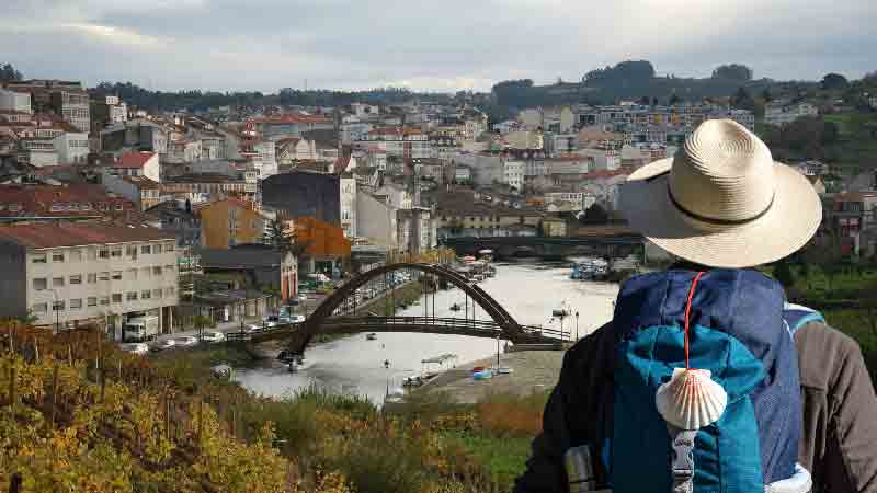 Pilgrim's arrival in Betanzos on the Camino Inglés Pilgrim overlooking the historic town of Betanzos, Galicia, with the Mandeo River and pedestrian bridge in view – a key stop on the English Way to Santiago