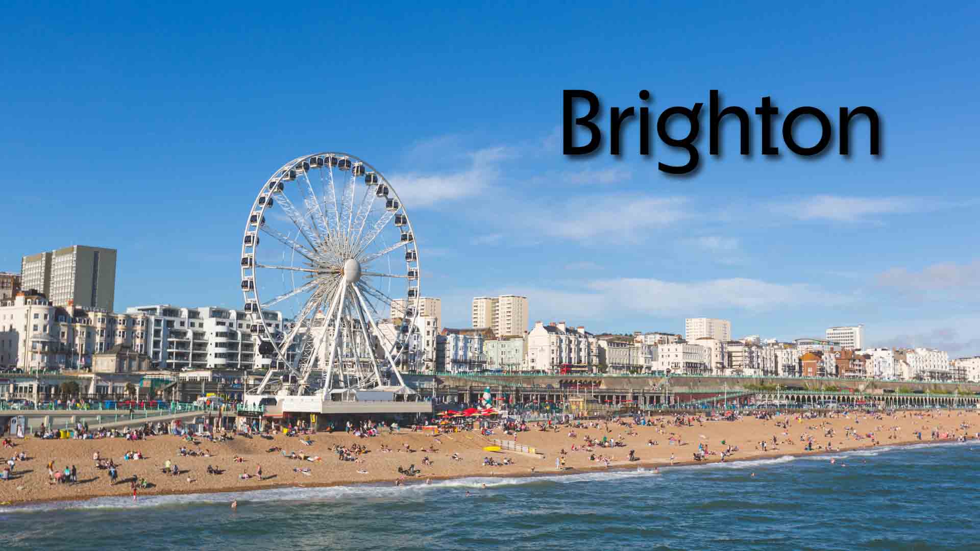 Brighton seafront with iconic Ferris wheel on a sunny day. Brighton beach with Ferris wheel and people enjoying the sunny seafront.