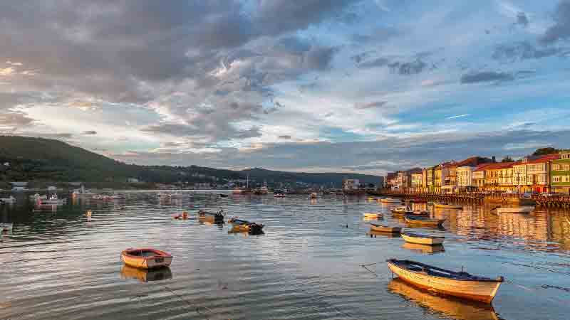 Sunset view of Ferrol’s waterfront and historic Galician houses along the estuary Colorful fishing boats moored in the peaceful waters of Ferrol, Spain, with traditional Galician houses reflecting the golden sunset