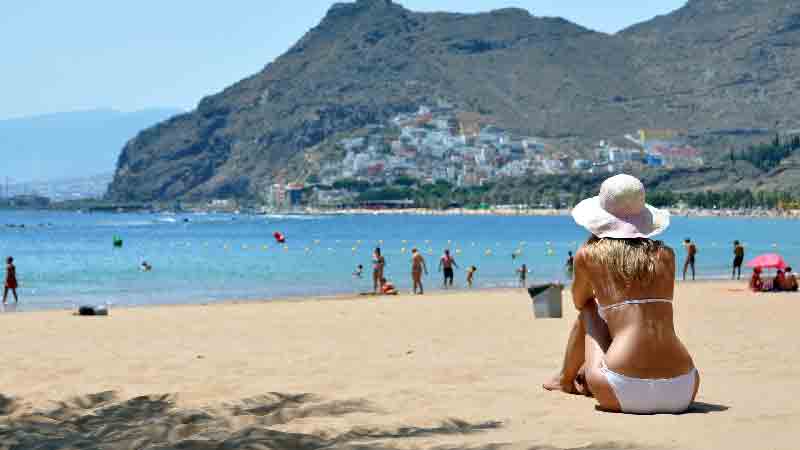 Las Teresitas Beach – Scenic view of southern Tenerife’s coast and mountains Woman sitting on golden sand at Las Teresitas beach overlooking the village and mountains in southern Tenerife