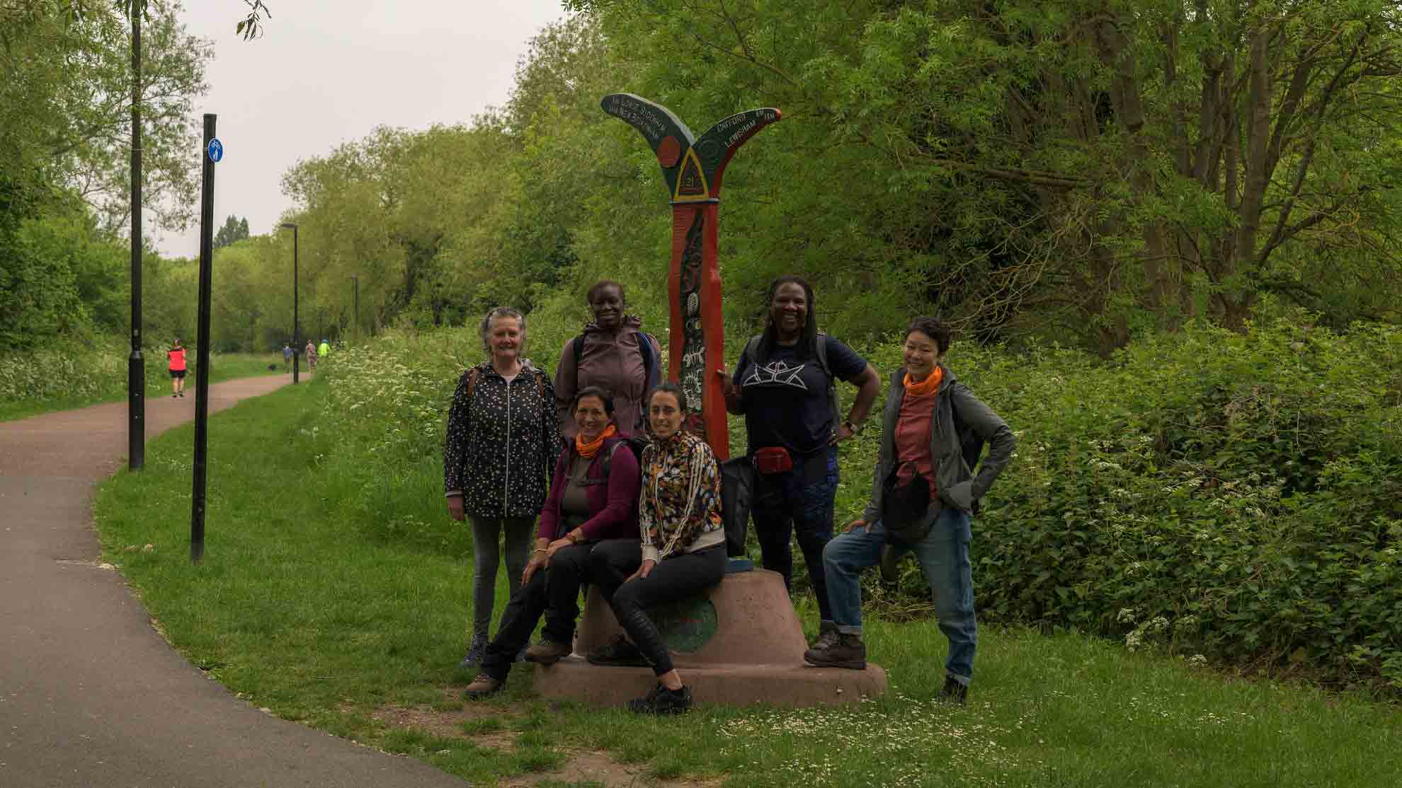Spartan hikers from Hiking in London Club on Waterlink Way trail, South London Group of women hikers from Hiking in London Club posing next to a red and green trail sign on Waterlink Way, surrounded by greenery and trees.