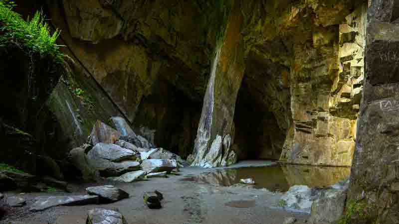 Cathedral Cave – Interior View, Lake District Hike Cathedral Cave interior with tall rock columns, mossy stones, and natural sunlight in the Lake District.