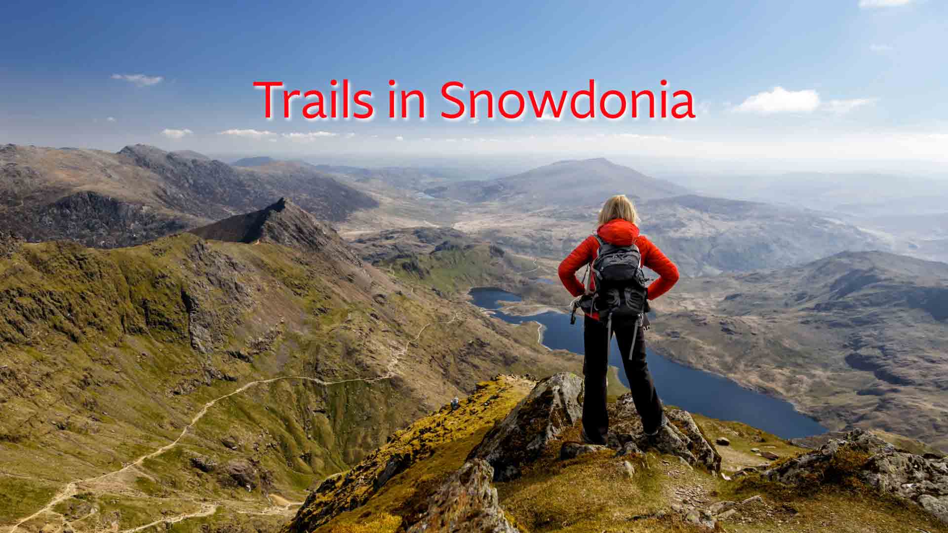 Hiker in red jacket with backpack admiring panoramic mountain views in Snowdonia National Park