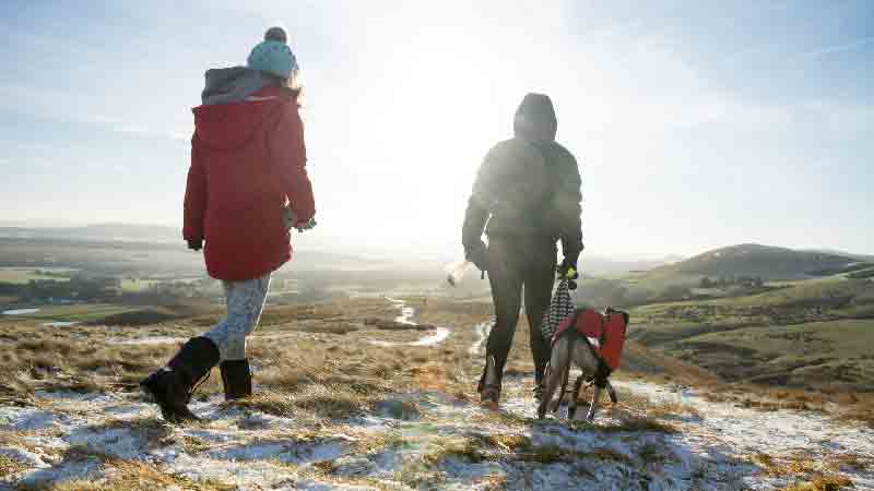 Winter hiking at Arthur’s Seat, Edinburgh Two people and a dog hiking on a snowy path at Arthur’s Seat with panoramic views of the Edinburgh countryside.
