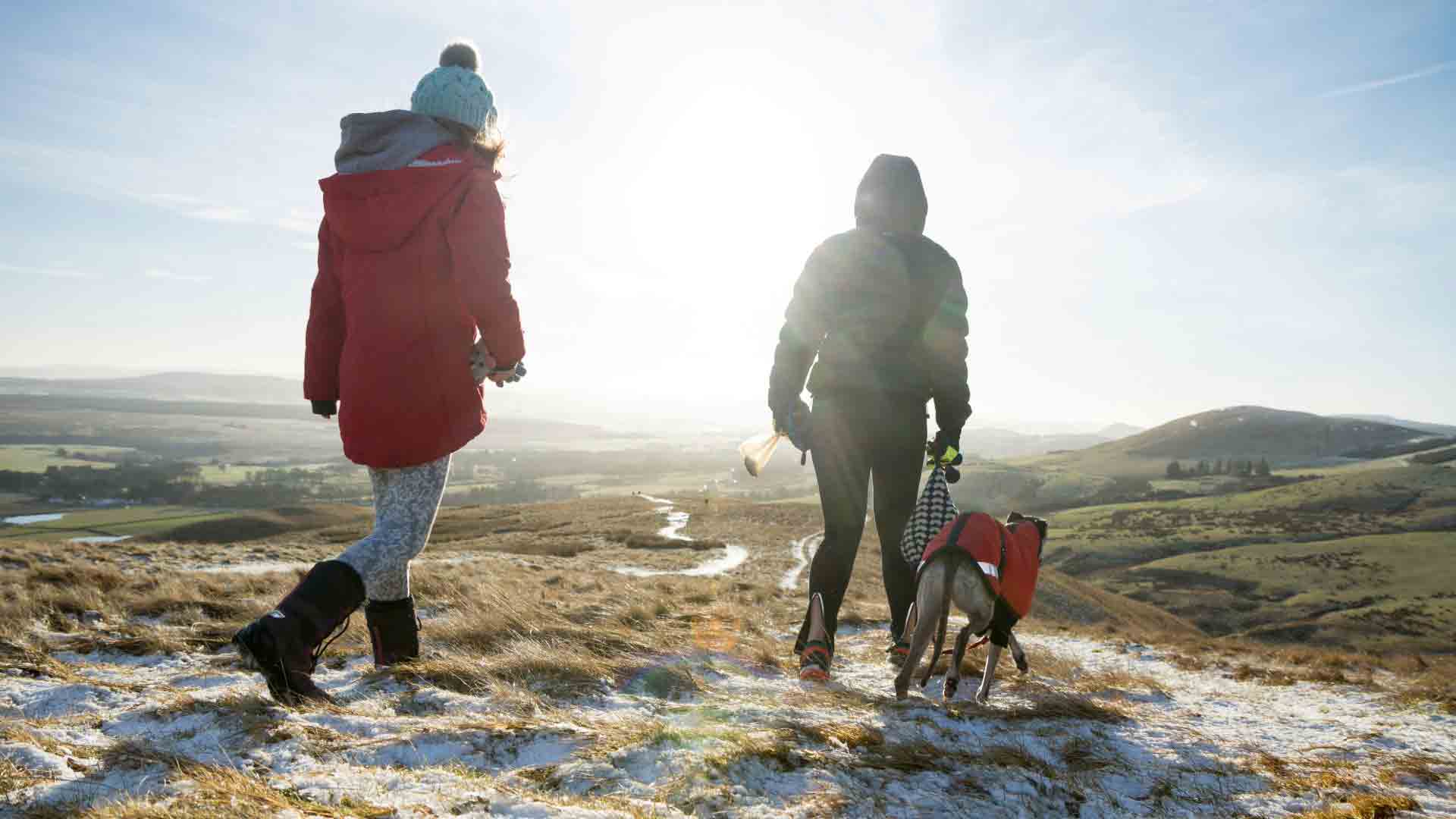 Winter hiking at Arthur’s Seat, Edinburgh Two people and a dog hiking on a snowy path at Arthur’s Seat with panoramic views of the Edinburgh countryside.