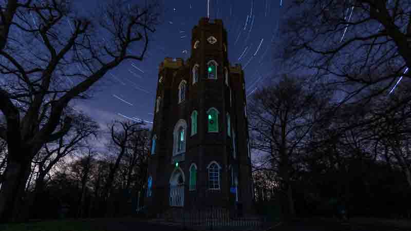 Severndroog Castle - A magical night view with star trails. Severndroog Castle illuminated at night, with a star-filled sky and light trails.