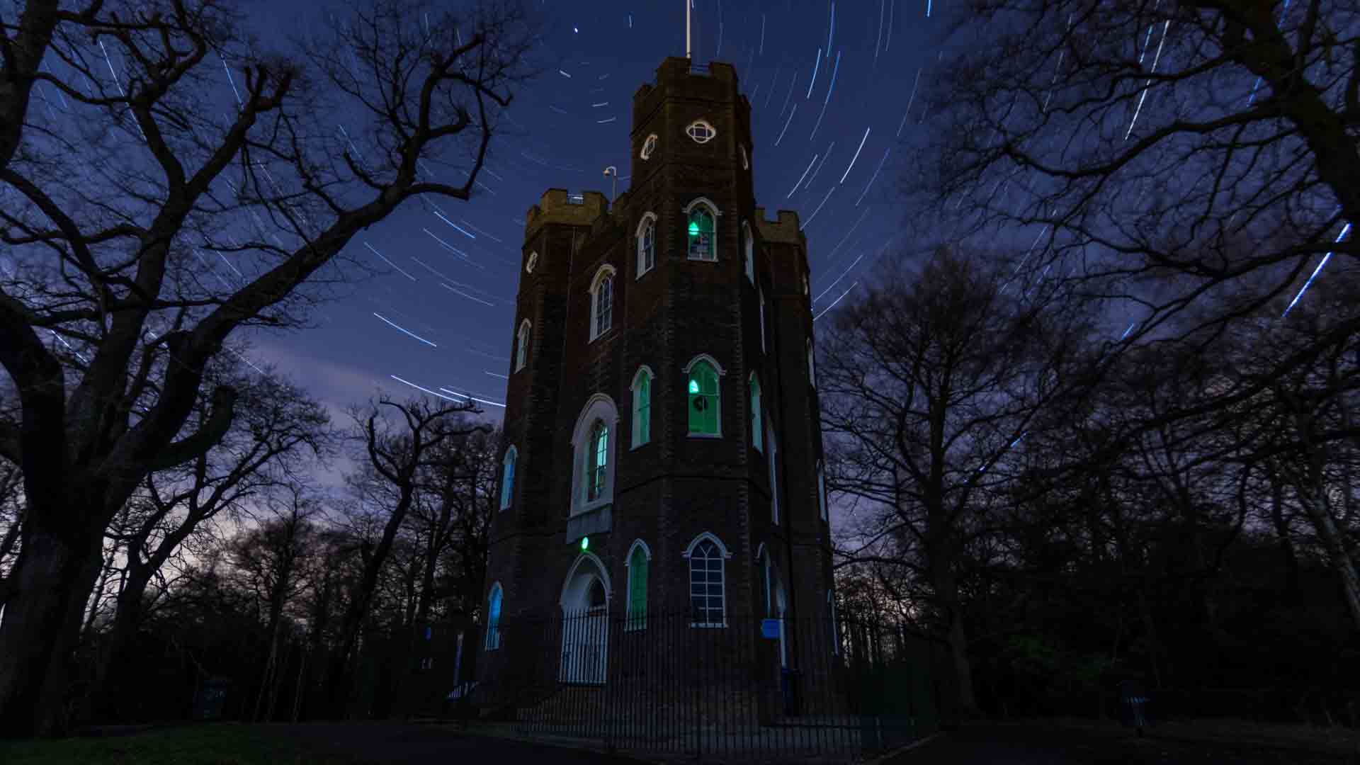 Severndroog Castle - A magical night view with star trails. Severndroog Castle illuminated at night, with a star-filled sky and light trails.