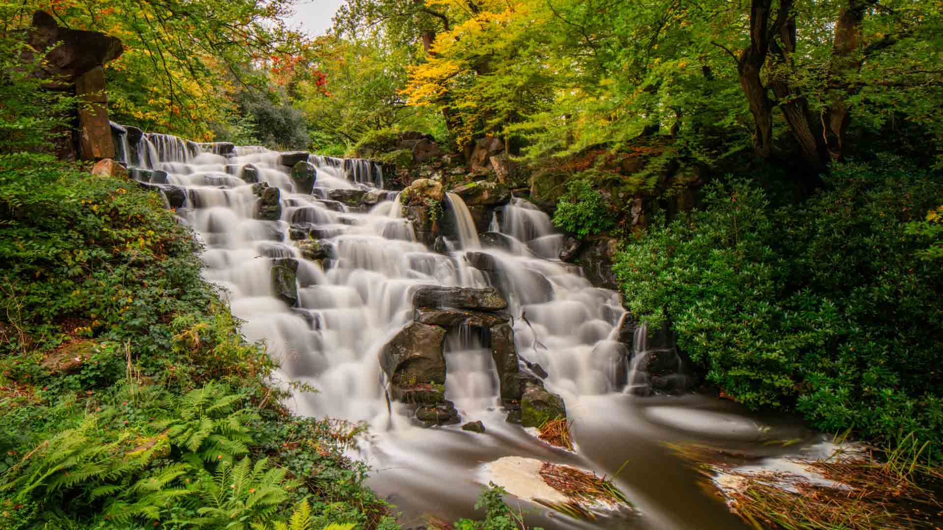 Cascading Waterfall at Virginia Water – A Scenic Highlight on the Circular Trail. Cascading waterfall surrounded by lush greenery at Virginia Water Circular trail.